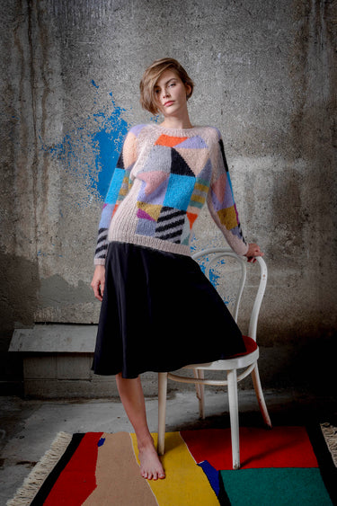 Woman wearing a mohair sweater. The sweater is beige and is covered with colourful abstract colour block patterns on most of its surface.